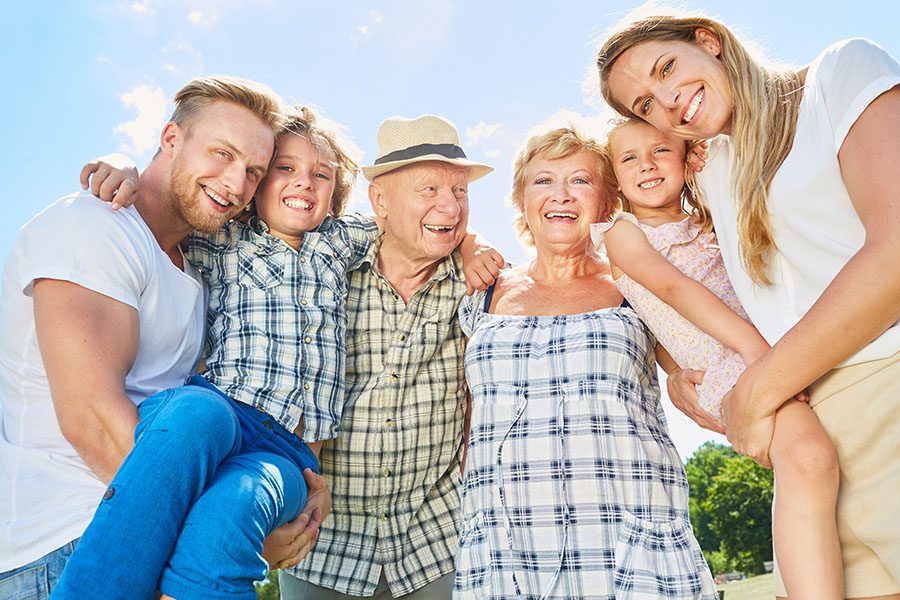 About Our Agency - View of Grandparents, Parents and Children Laughing and Smiling While Embracing Each Other on a Sunny Day